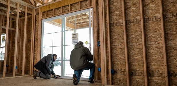 two men installing a sliding patio door in a home under new construction