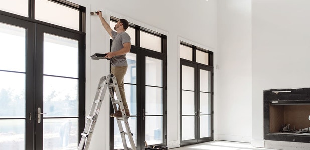 three large hinged patio doors along a wall while a painter finishes the walls around the doors