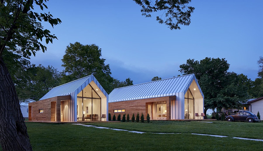 Modern white home at dusk all lit up through floor-to-ceiling fixed windows