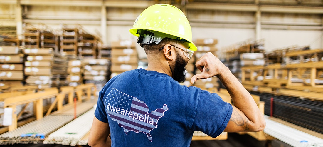 a pella employee pausing to smile at the camera while working on a large piece of glass