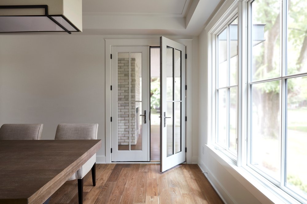 White farmhouse style dining room with wood flooring, double-hung windows on the right, and a set of white french doors open