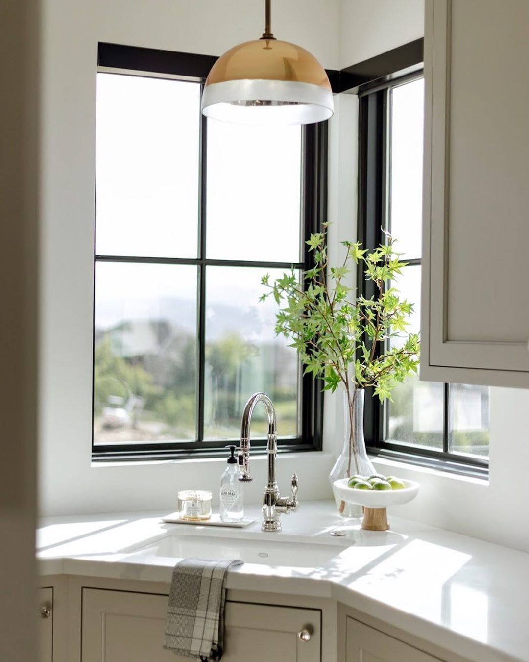 corner kitchen sink with a fixed black window on either side and brass pendant directly above