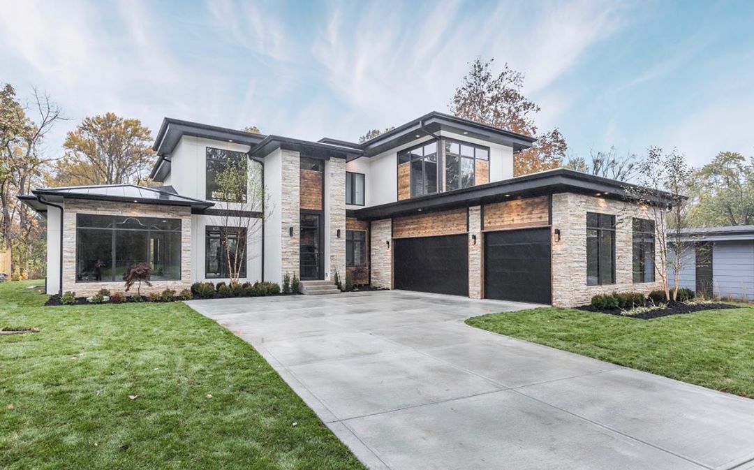 modern home featuring a mix of tan stone, white stucco, and black accents including black windows