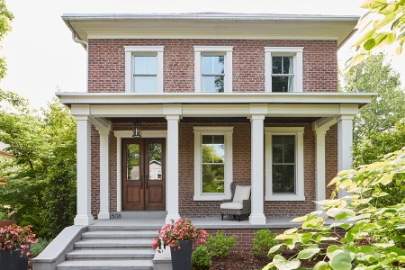 Two Story gray siding home with wood entry door and white framed windows with grilles