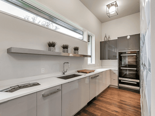 White on white long galley kitchen with cabinets along the wall and a long rectangle shaped window overhead